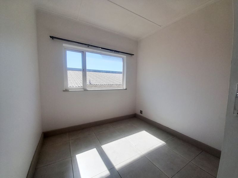 An empty bedroom featuring neutral tiled flooring, white walls, and a window with a fitted curtain rod.