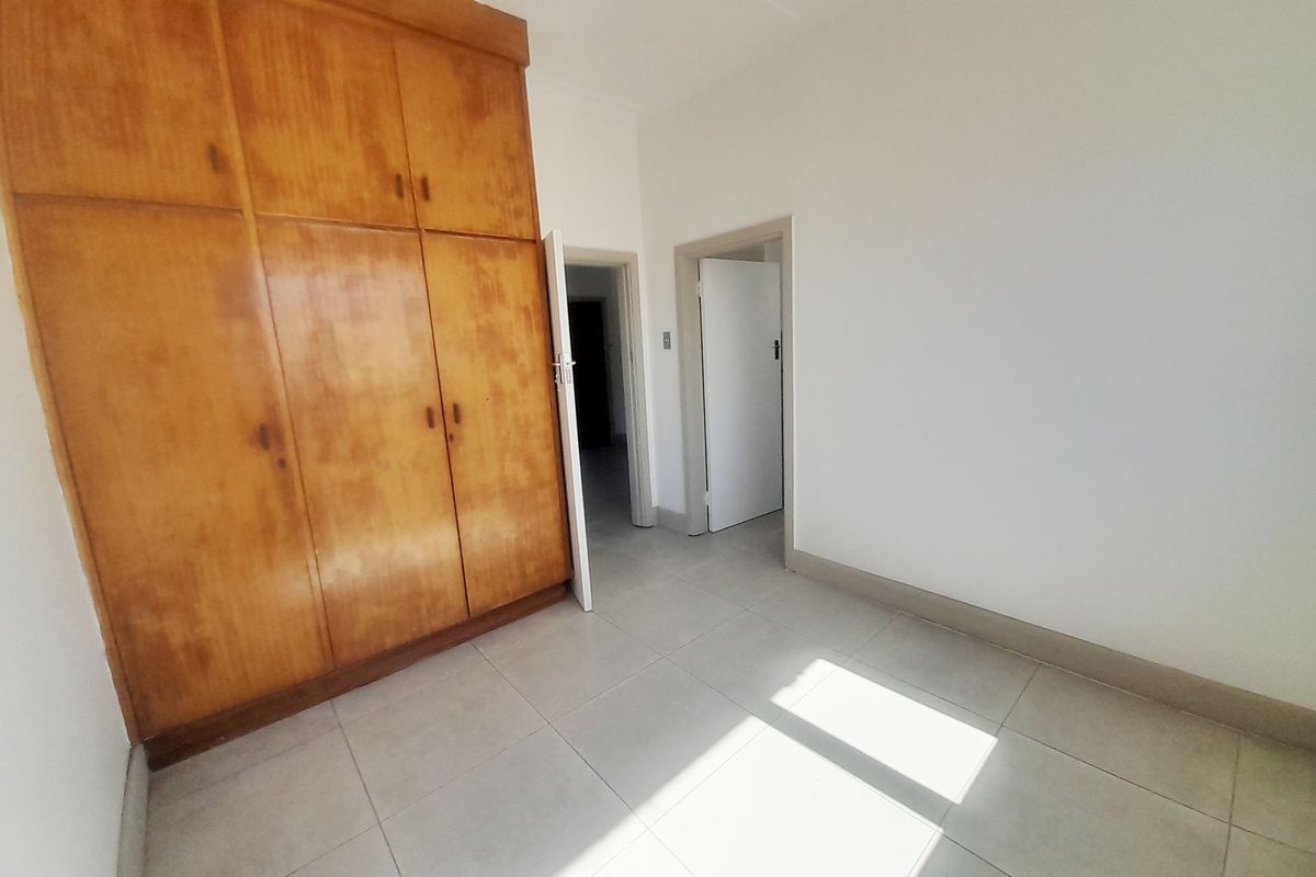 An empty bedroom featuring tiled flooring and large built-in wooden cupboards, offering a neutral space ready for personalization.
