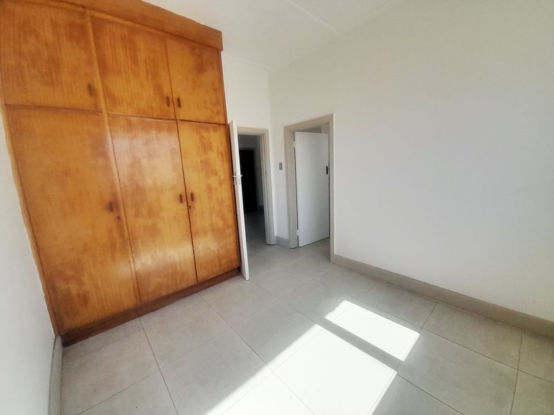 An empty bedroom featuring tiled flooring and large built-in wooden cupboards, offering a neutral space ready for personalization.