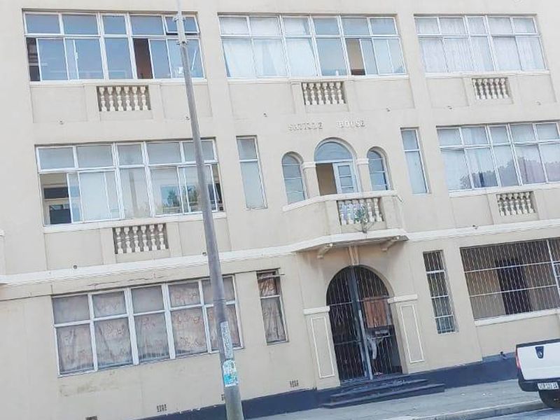 Street-facing view of a multi-story apartment building featuring classic architectural details, arched entrance, and multiple balconies.