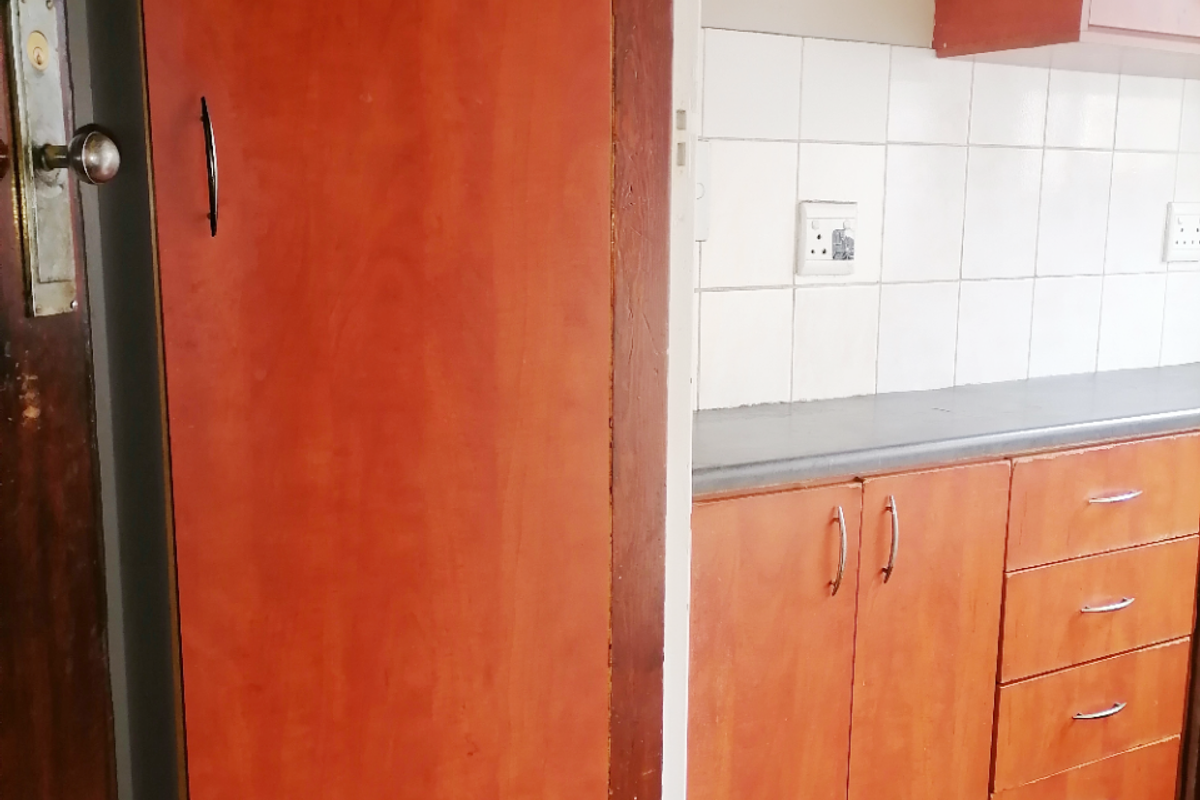 A compact kitchen area featuring dated timber-look cabinetry, a neutral tiled backsplash, and worn timber flooring, offering potential for a modern renovation.