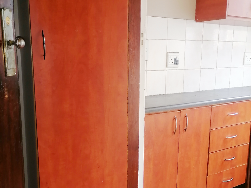 A compact kitchen area featuring dated timber-look cabinetry, a neutral tiled backsplash, and worn timber flooring, offering potential for a modern renovation.