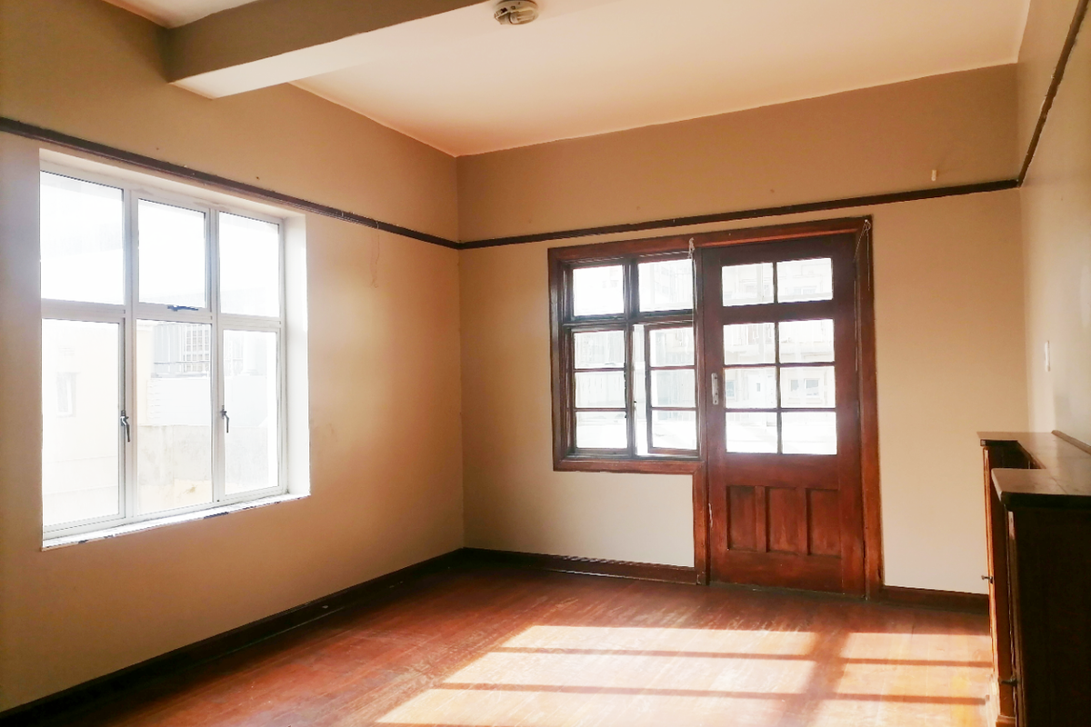 An empty living room featuring original hardwood flooring, timber-framed windows, and a classic timber door, offering a blank canvas for renovation.