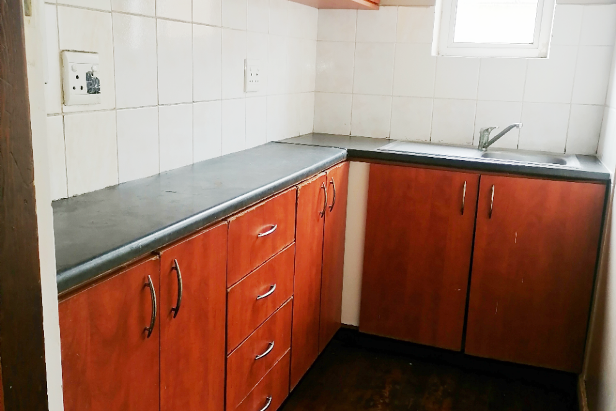 A compact kitchen featuring timber flooring, laminate cabinetry, tiled backsplash, and a stainless steel sink, offering a functional space ready for updates.