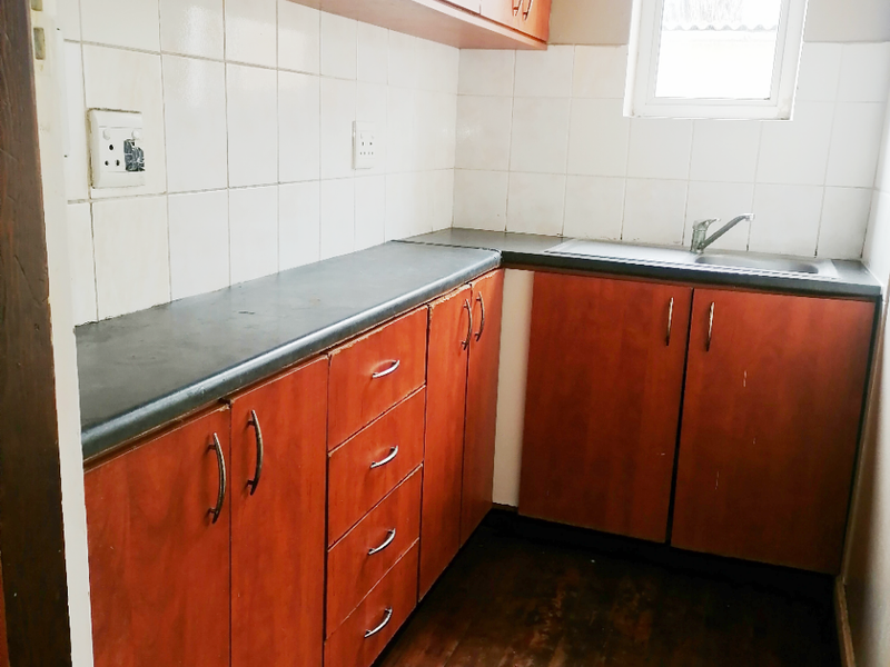 A compact kitchen featuring timber flooring, laminate cabinetry, tiled backsplash, and a stainless steel sink, offering a functional space ready for updates.