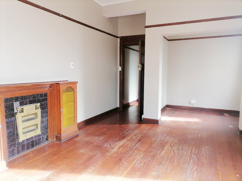 An empty living room featuring original hardwood flooring, a built-in fireplace with decorative tiling, and classic timber picture rails.