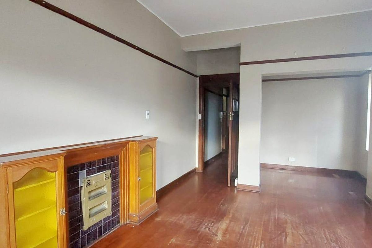 An empty living room featuring original hardwood flooring, a built-in fireplace with display cabinets, and classic picture rail detailing.