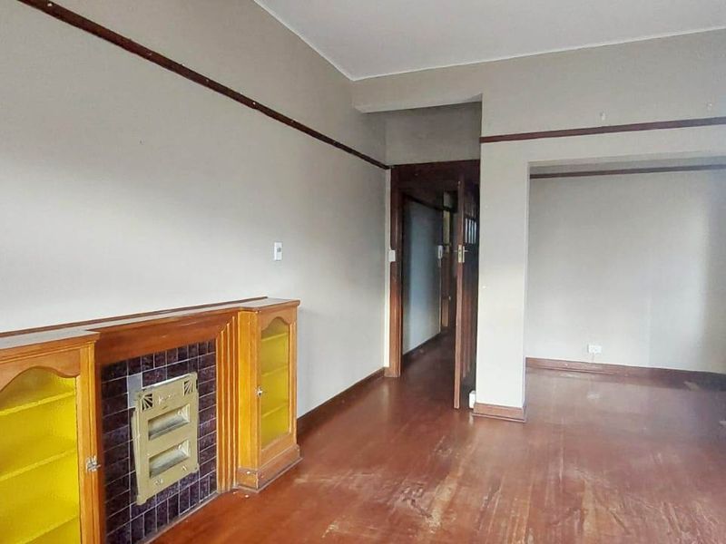 An empty living room featuring original hardwood flooring, a built-in fireplace with display cabinets, and classic picture rail detailing.
