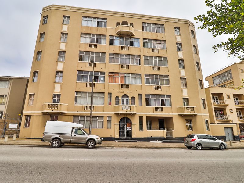 A multi-story apartment building facade featuring classic architectural details, arched entrance, and multiple balconies, situated along a street front.