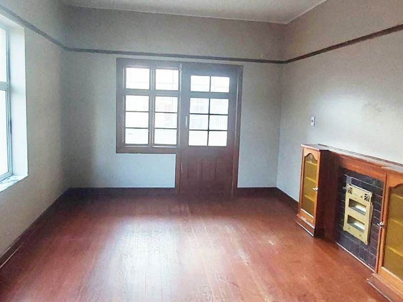 An empty living room featuring original hardwood flooring, a built-in fireplace with flanking cabinetry, and large multi-pane windows providing natural light.