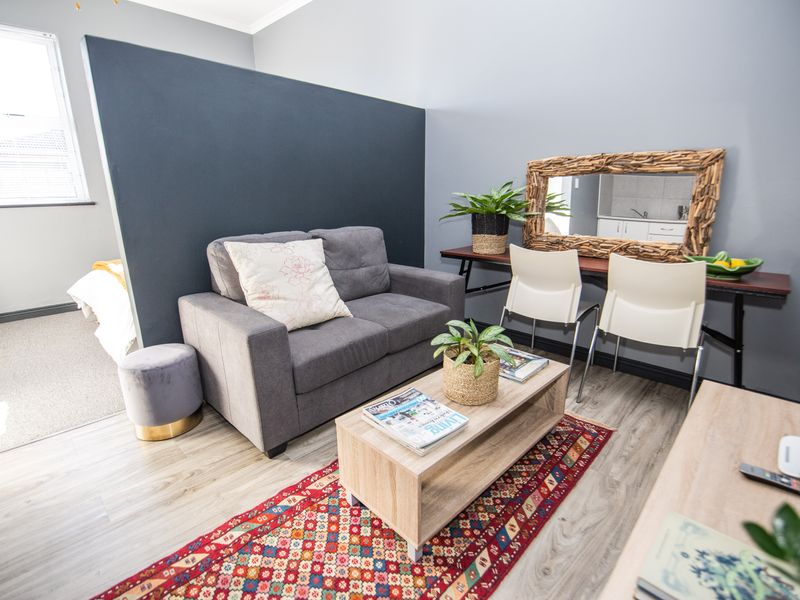 An open-plan living area featuring modern laminate flooring, a dark accent partition wall, and a bright window, creating a functional and contemporary living space.