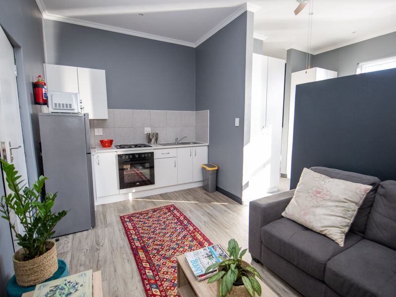 An open-plan living area featuring a compact kitchen with built-in cabinetry, oven, hob, and sink, complemented by modern laminate flooring and neutral grey walls.