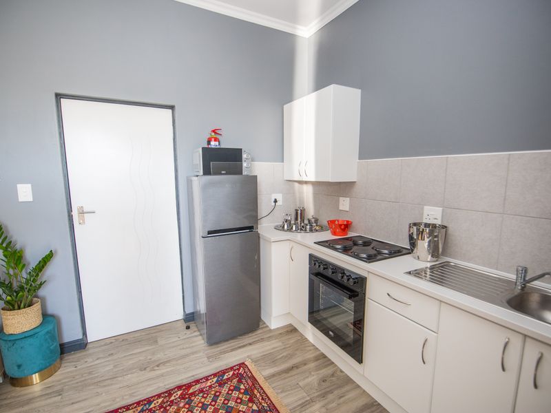 A compact, functional kitchen featuring white cabinetry, a tiled backsplash, built-in oven with electric hob, and stainless steel sink, finished with modern laminate flooring.