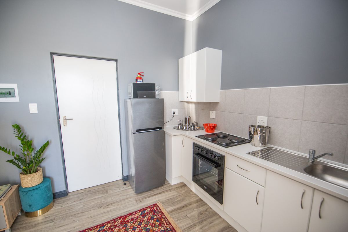 A compact, functional kitchen featuring white cabinetry, a tiled backsplash, built-in oven with electric hob, and stainless steel sink, finished with modern laminate flooring.