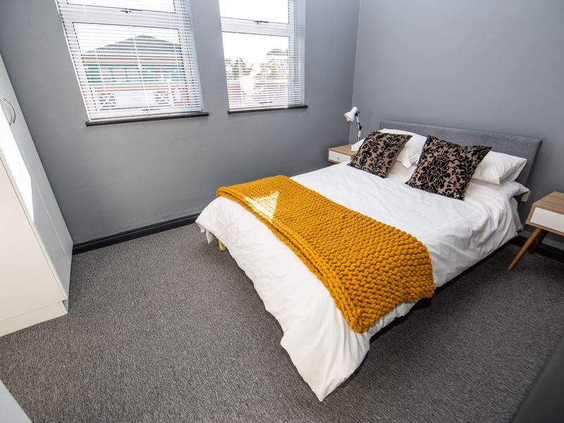 A well-maintained bedroom featuring grey carpeting, neutral wall tones, and built-in wardrobe storage, complemented by dual windows with fitted venetian blinds.