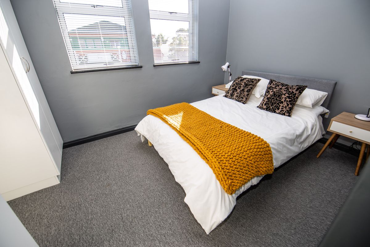 A well-maintained bedroom featuring grey carpeting, neutral wall tones, and built-in wardrobe storage, complemented by dual windows with fitted venetian blinds.