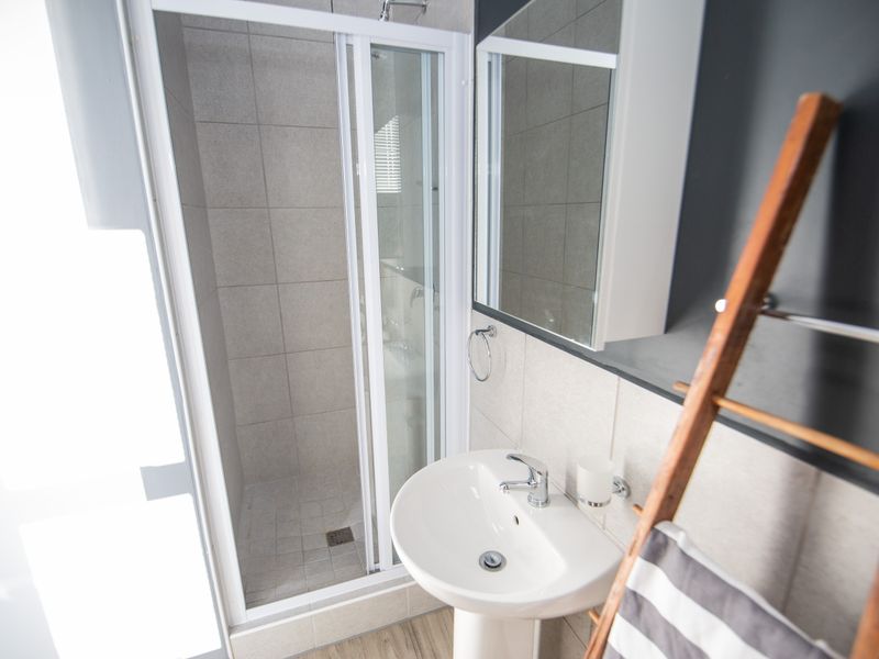 A modern bathroom featuring a glass-enclosed shower, pedestal basin with mixer tap, and wall-mounted medicine cabinet with neutral tiling.