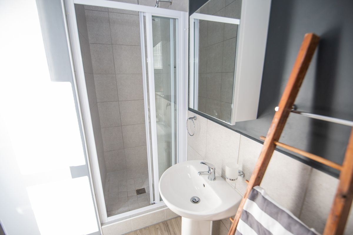 A modern bathroom featuring a glass-enclosed shower, pedestal basin with mixer tap, and wall-mounted medicine cabinet with neutral tiling.
