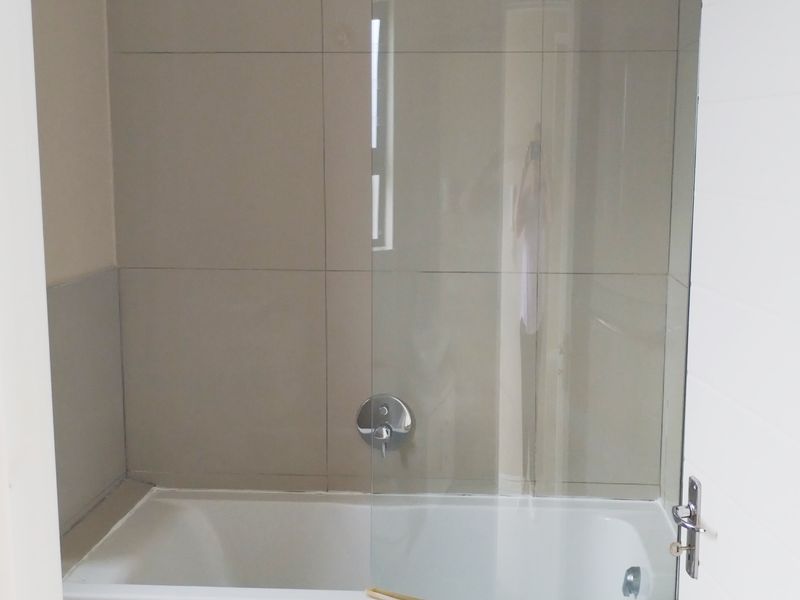 A clean bathroom featuring a bathtub with a glass shower screen, overhead shower fixture, and neutral wall tiling.