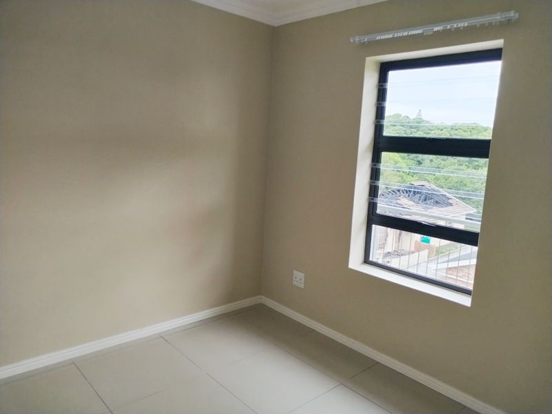 A clean, empty bedroom featuring neutral wall tones, tiled flooring, and a large aluminium window with a view of the surrounding area.