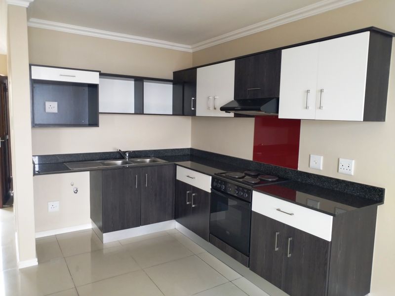 Modern kitchen featuring two-tone cabinetry, granite countertops, integrated oven and hob, and a striking red glass splashback in a clean, open-plan layout.
