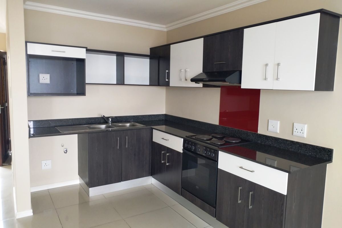 Modern kitchen featuring two-tone cabinetry, granite countertops, integrated oven and hob, and a striking red glass splashback in a clean, open-plan layout.