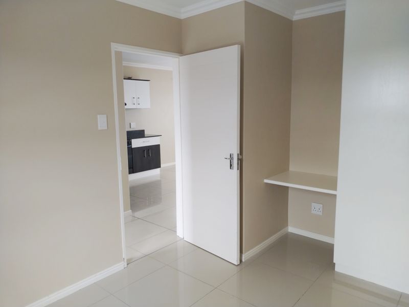 A clean, neutral hallway featuring tiled flooring, a built-in desk nook, and a view through to the kitchen area.