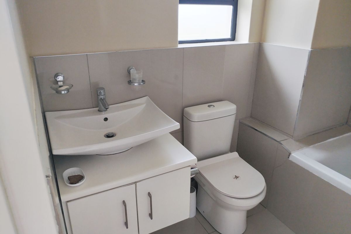 A functional bathroom featuring a modern vanity with basin, a standard toilet, and a tiled bathtub surround with neutral wall and floor tiles.