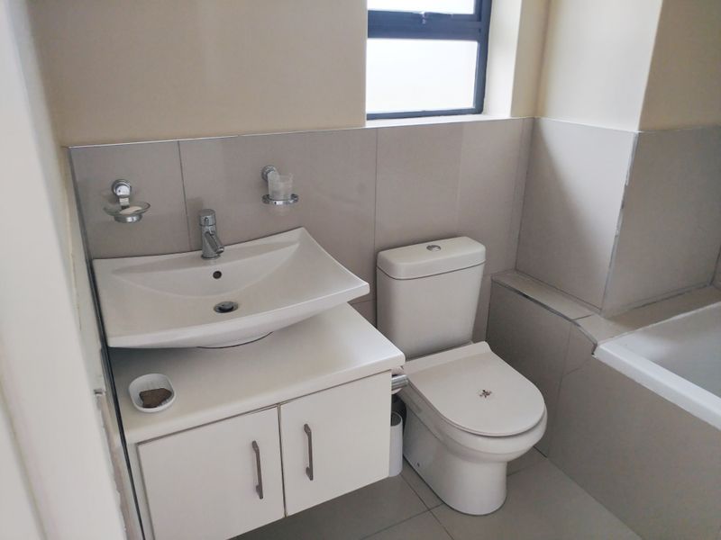 A functional bathroom featuring a modern vanity with basin, a standard toilet, and a tiled bathtub surround with neutral wall and floor tiles.