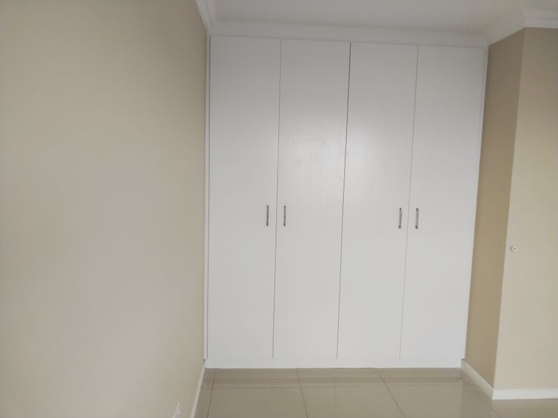 A clean, empty bedroom featuring neutral walls, tiled flooring, and ample built-in cupboard storage.