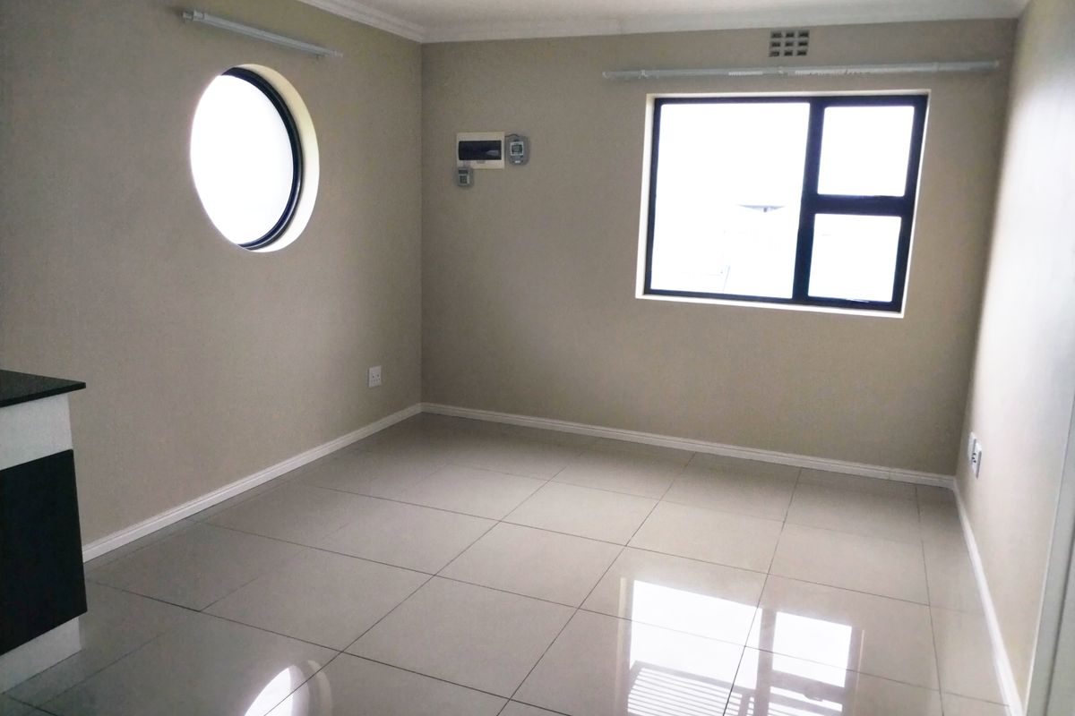 A bright, empty living area featuring polished porcelain floor tiles, a unique circular window, and a standard rectangular window with neutral wall finishes.