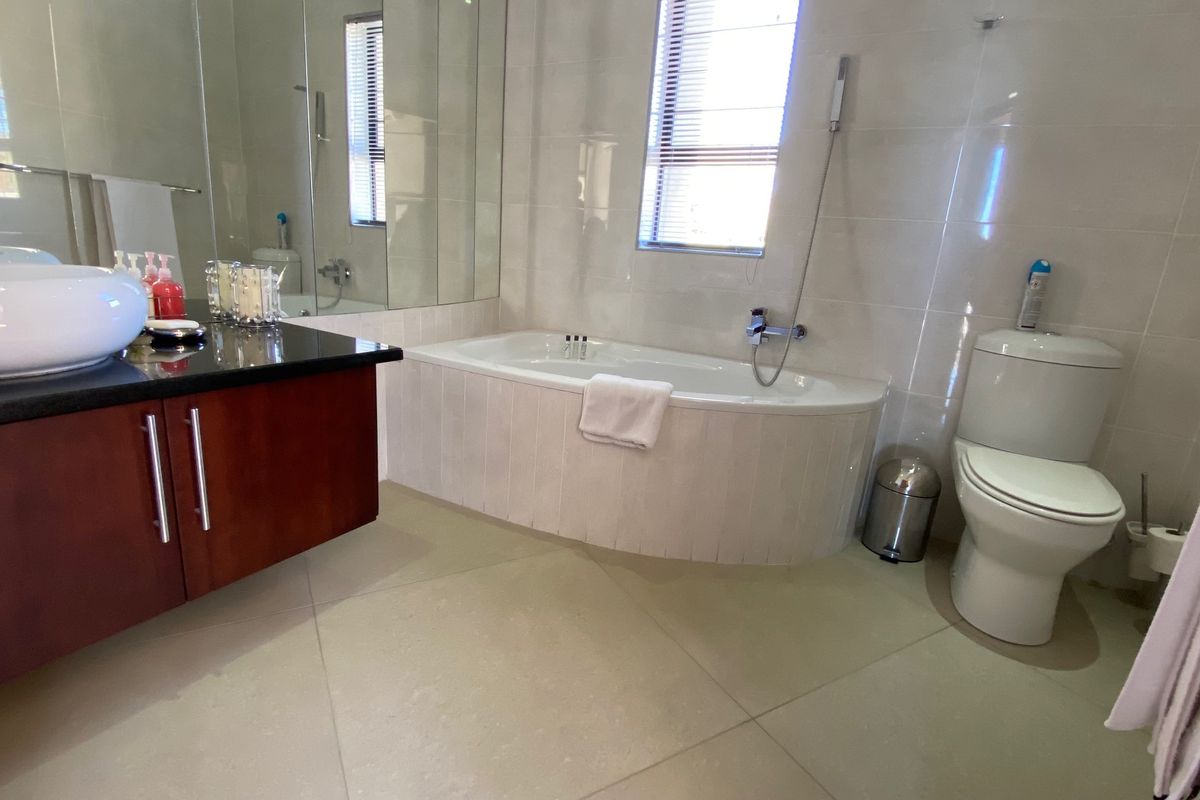 A well-maintained bathroom featuring a built-in bathtub, a modern vanity with a vessel sink, a toilet, and large-format floor tiles.