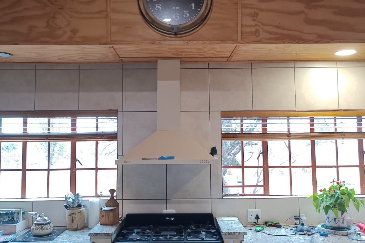 A rustic kitchen featuring a vintage-style gas range, stainless steel extractor fan, granite countertops, and plywood ceiling paneling with large windows.
