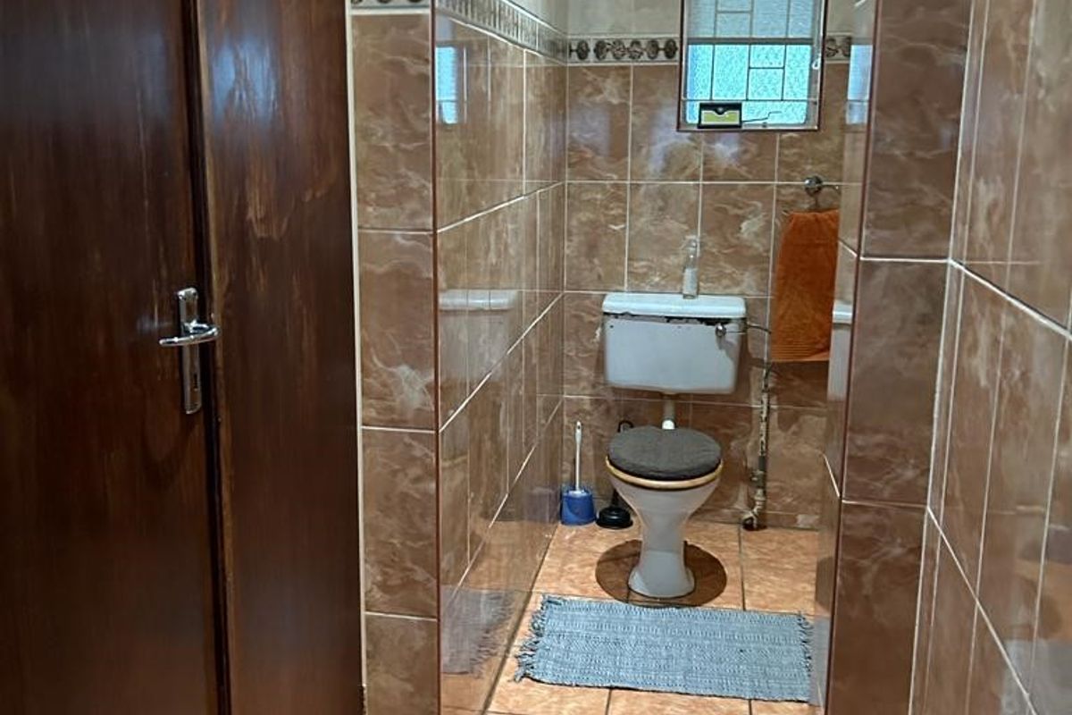 A functional bathroom featuring floor-to-ceiling ceramic tiling, a standard toilet, and built-in wooden cabinetry for storage.