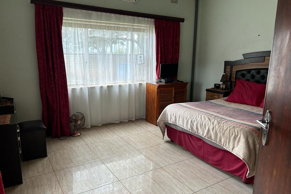 A spacious bedroom featuring tiled flooring, a wall-mounted air conditioning unit, and large windows with curtain tracks.