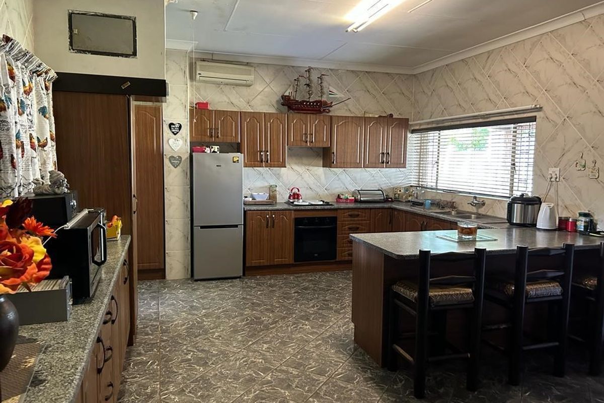 Spacious kitchen featuring wooden cabinetry, granite countertops, a central island, and integrated oven with hob.