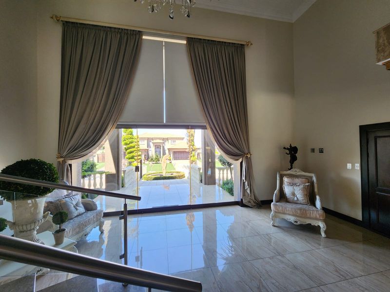 Spacious grand entrance hall featuring high ceilings, polished porcelain floor tiles, a crystal chandelier, and large glass sliding doors opening to the exterior.