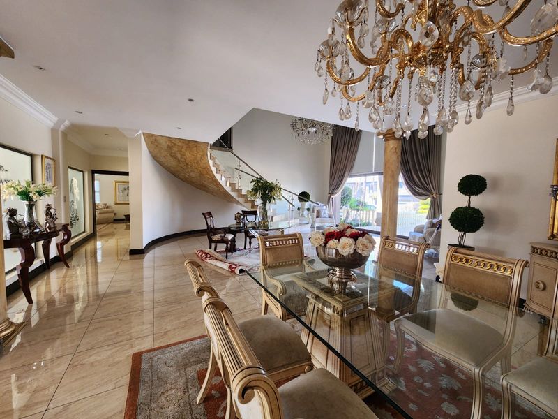 Spacious open-plan living and dining area featuring a grand curved staircase, elegant crystal chandelier, and polished tiled flooring throughout.