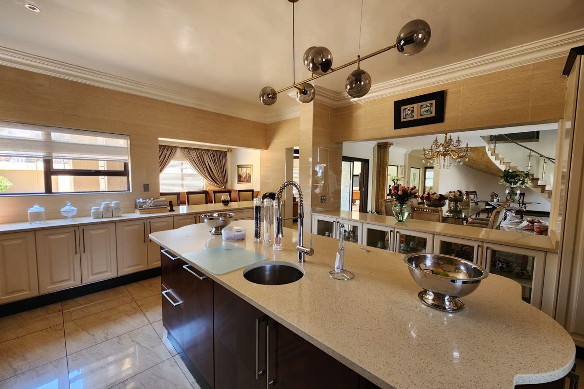 Spacious modern kitchen featuring a large central island with stone countertops, integrated cabinetry, and elegant pendant lighting, seamlessly connecting to the dining and living areas.