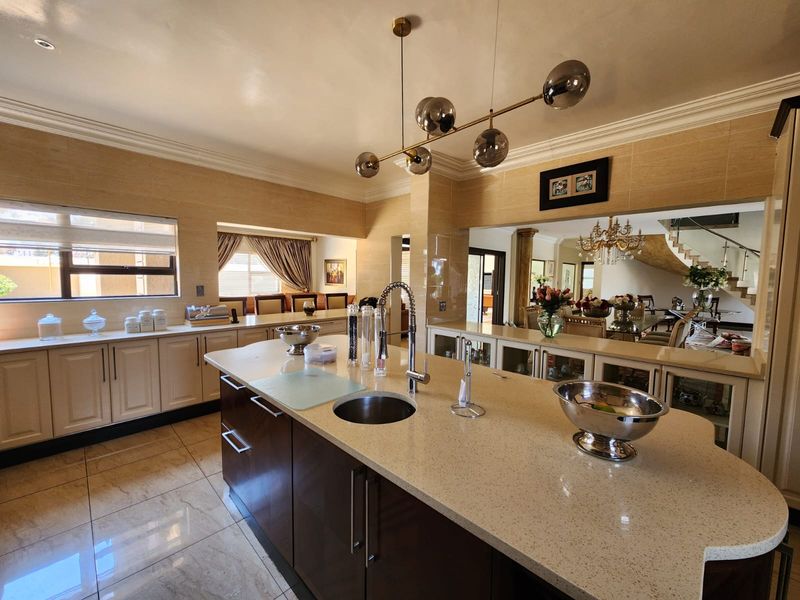 Spacious modern kitchen featuring a large central island with stone countertops, integrated cabinetry, and elegant pendant lighting, seamlessly connecting to the dining and living areas.