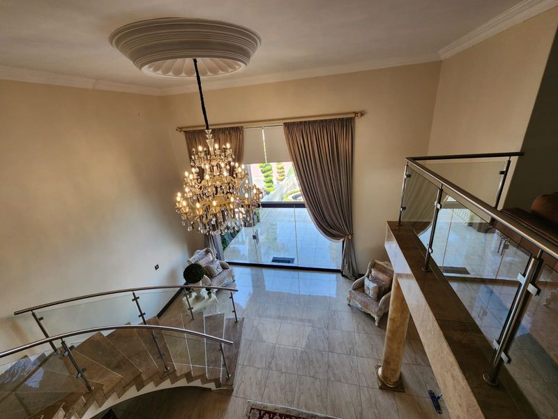 Grand entrance foyer featuring a curved staircase with glass balustrades, polished marble flooring, and a decorative ceiling medallion with a crystal chandelier.