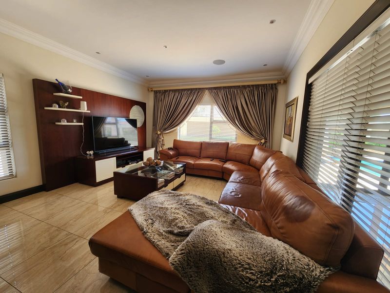 A well-maintained living room featuring tiled flooring, recessed downlighting, ceiling coving, and a custom built-in media unit with integrated shelving.