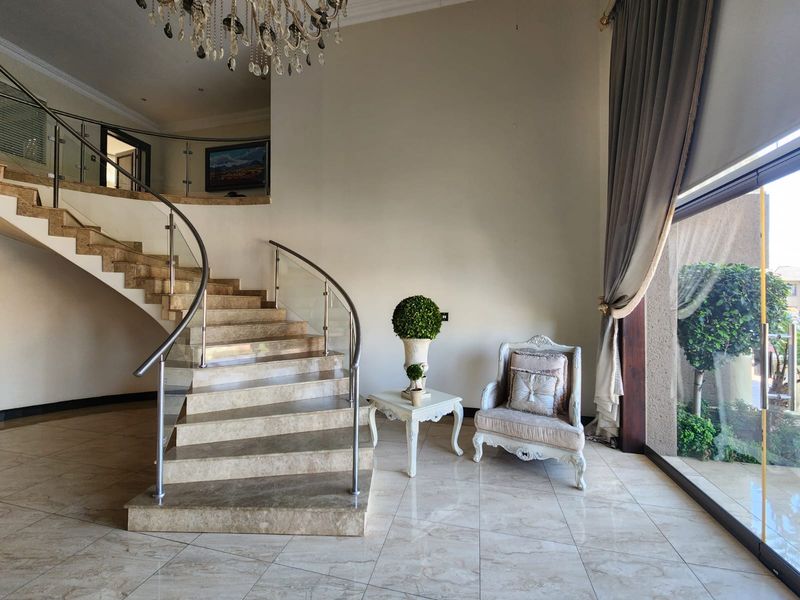 Elegant entrance hall featuring a grand curved marble staircase with glass balustrades, polished marble flooring, and a large sliding door providing natural light.