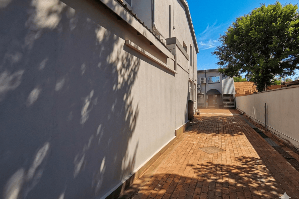 A paved side walkway leading to the rear of the business premises, featuring a clean brick surface and exterior building walls.