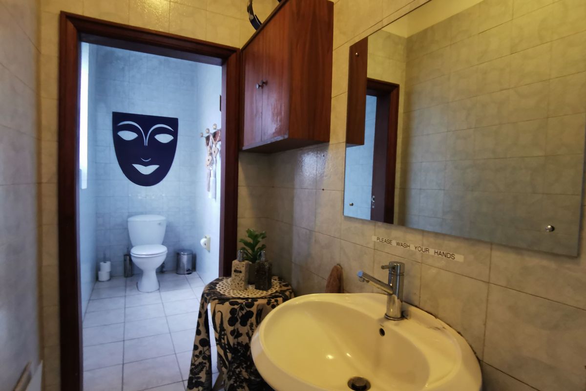 A functional bathroom featuring a wall-mounted basin, mirror, and overhead storage cabinet, with an adjoining toilet area.