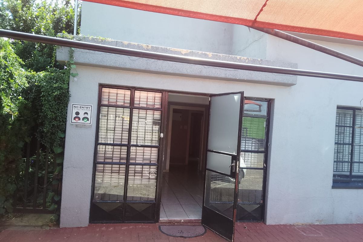 Exterior view of a commercial building entrance featuring metal-framed glass doors, a paved walkway, and an overhead shade structure.