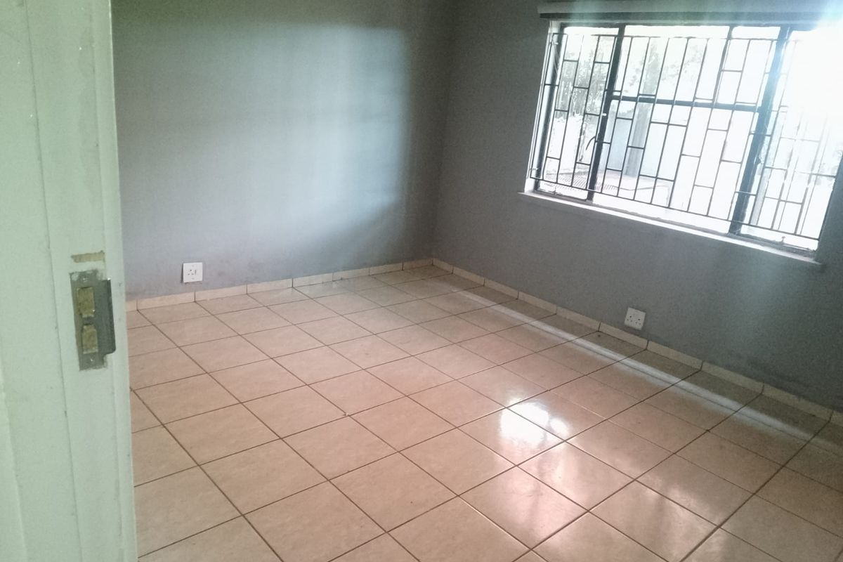 A vacant room featuring neutral tiled flooring, grey painted walls, and a window fitted with security bars.