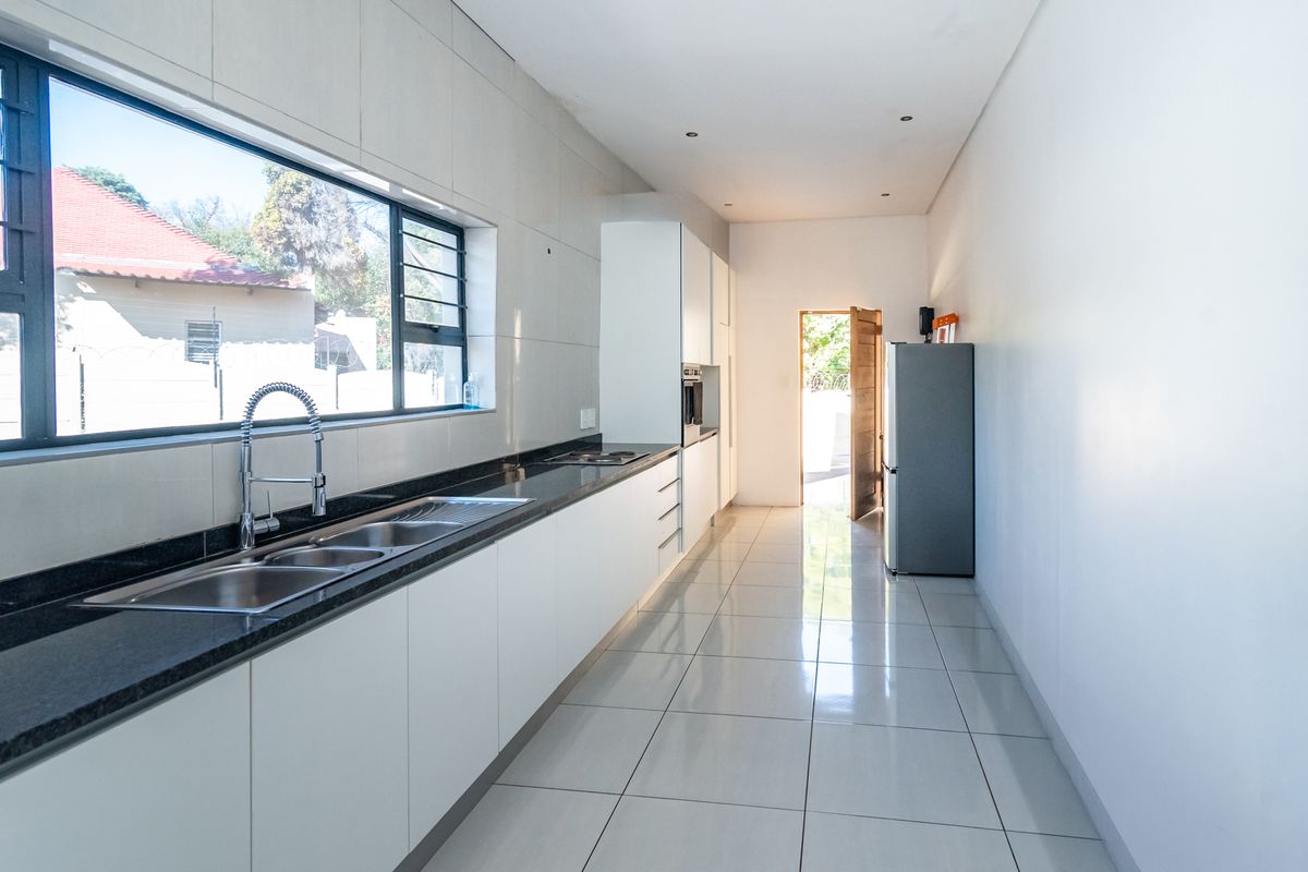A modern, galley-style kitchen featuring sleek white cabinetry, dark granite countertops, a stainless steel double sink, and polished floor tiles.