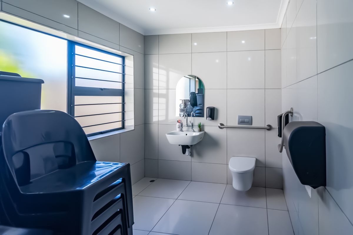 A clean, modern commercial restroom featuring wall-mounted toilet, basin, stainless steel grab rail, and tiled finishes throughout.
