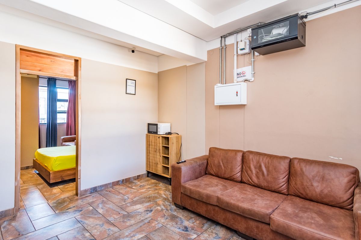 A functional living area featuring tiled flooring, exposed electrical infrastructure, and a doorway leading to an adjacent bedroom space.